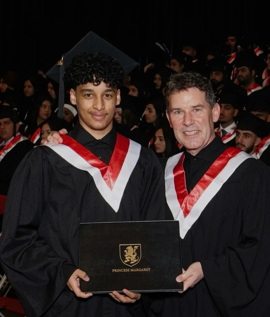 Ammar at his high school graduation, holding a graduation folder alongside another person