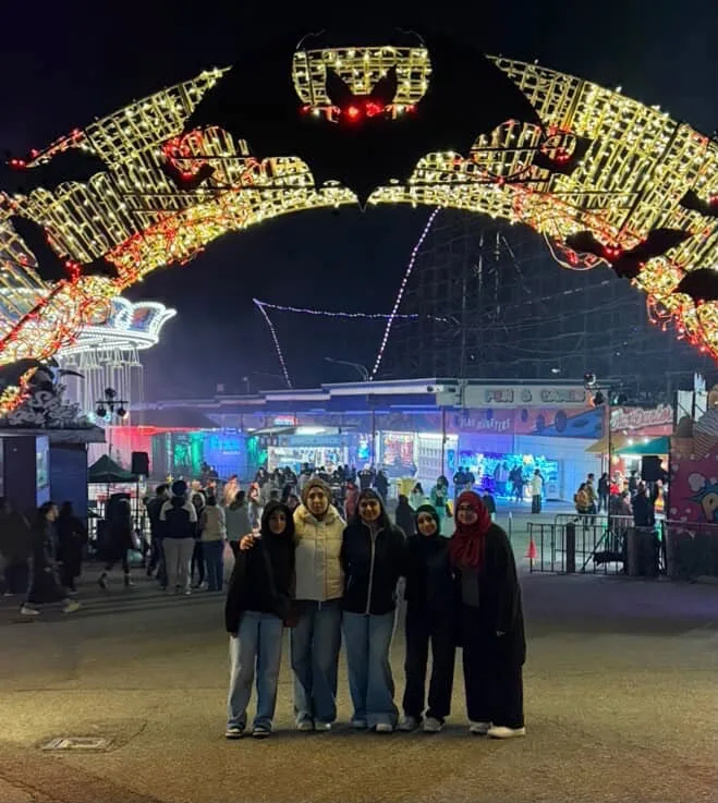 Five people together beneath illuminated amusement park rides at night