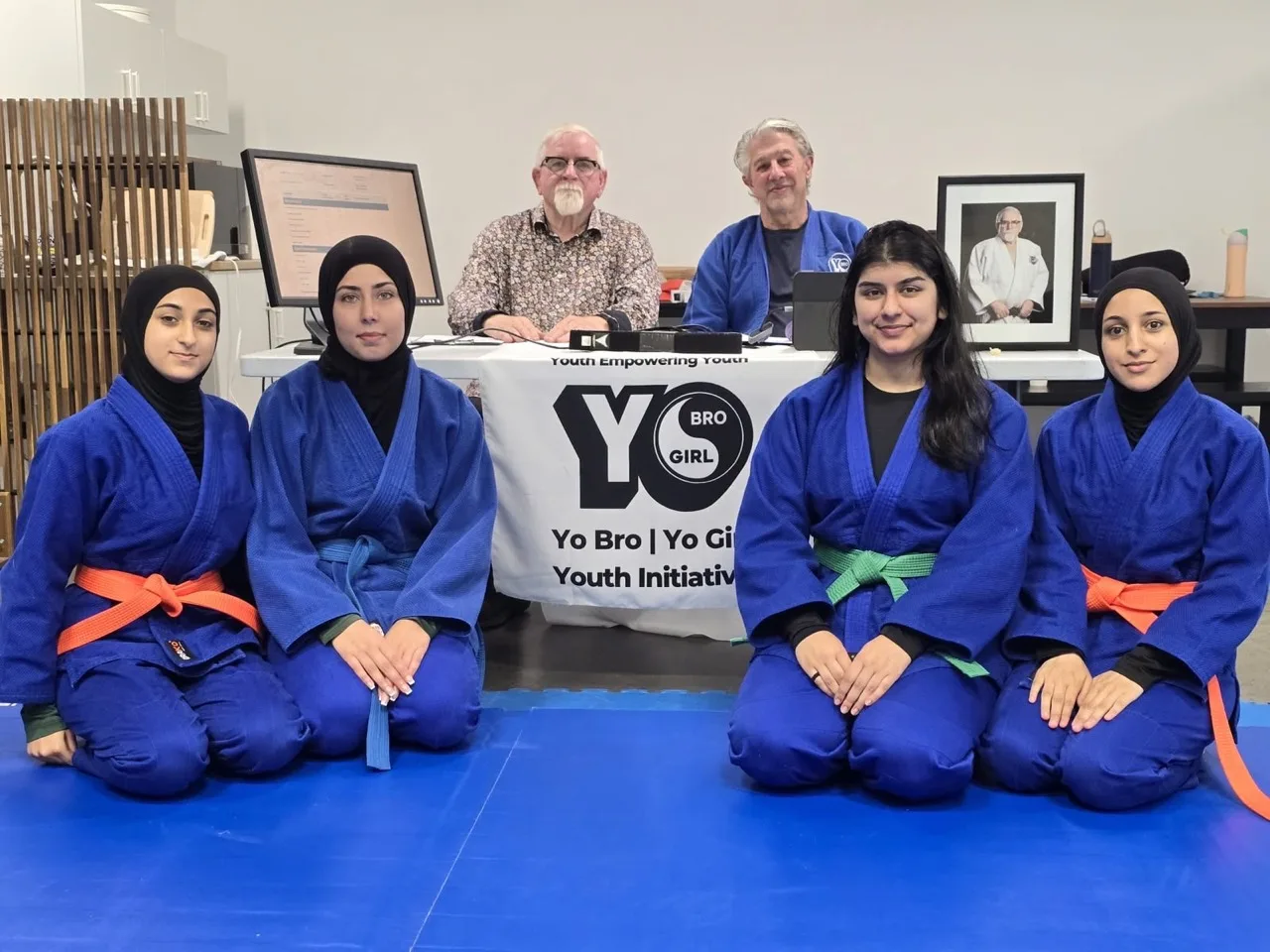 Four martial arts participants in blue uniforms with instructors behind them at YBYG