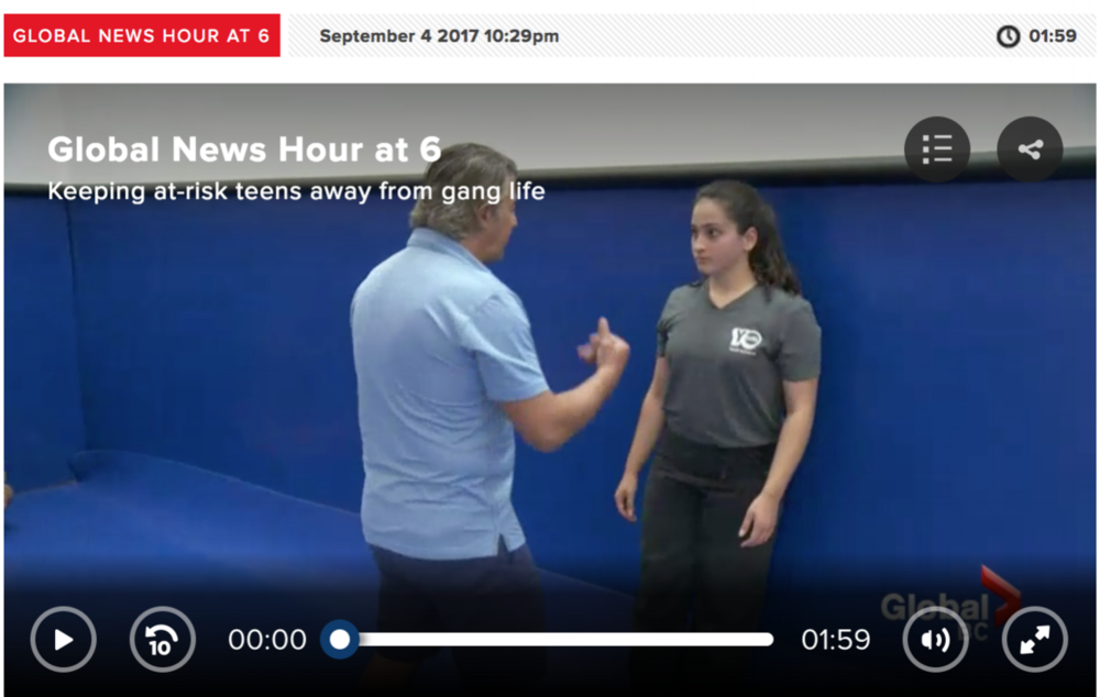 A man gestures while speaking to a young woman in a grey t-shirt about keeping away from gang life, in a blue-walled room during the global news hour at 6 broadcast.